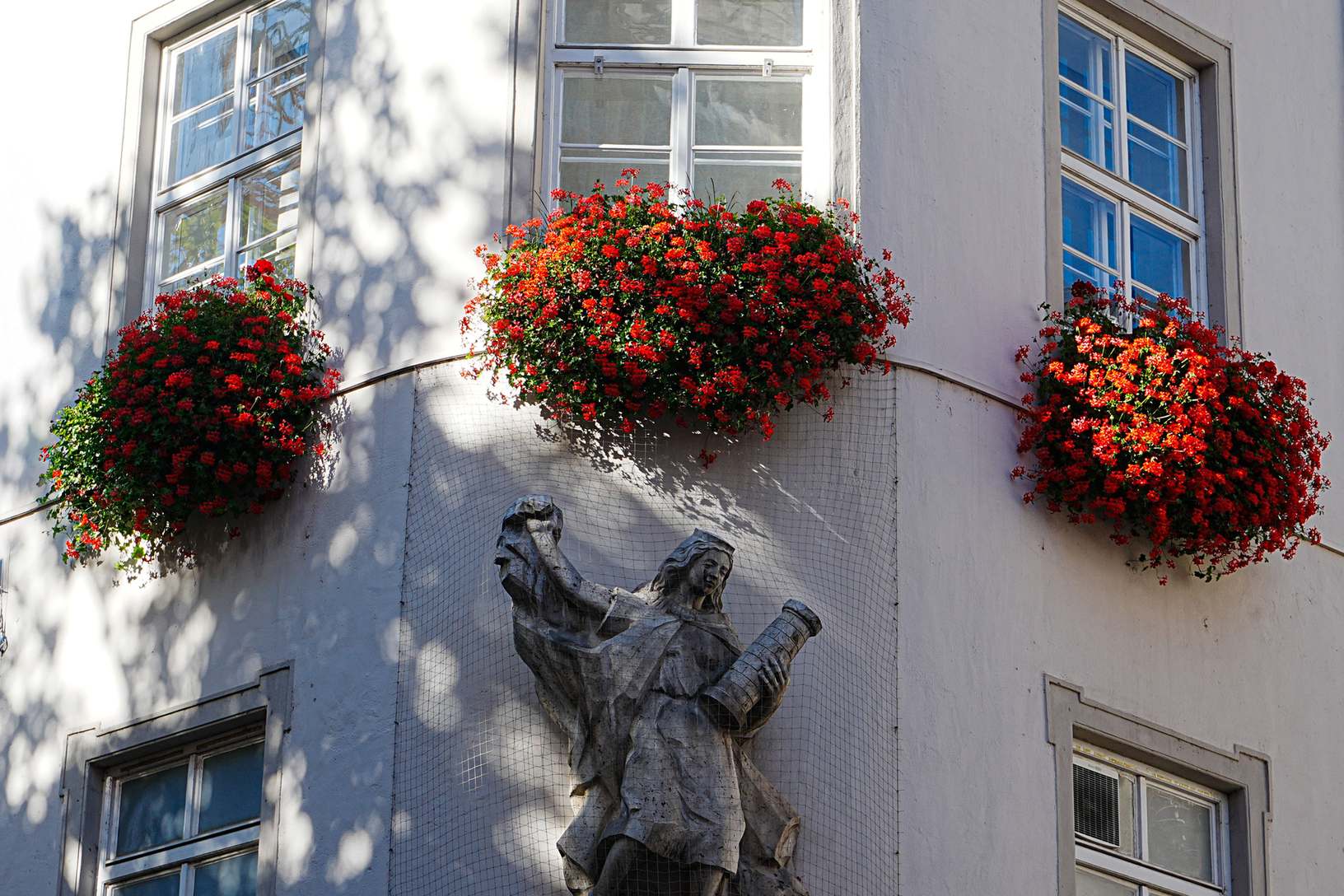 Münchner Straßenfassade mit Steinskulptur und Blumen an einem historischen Gebäude